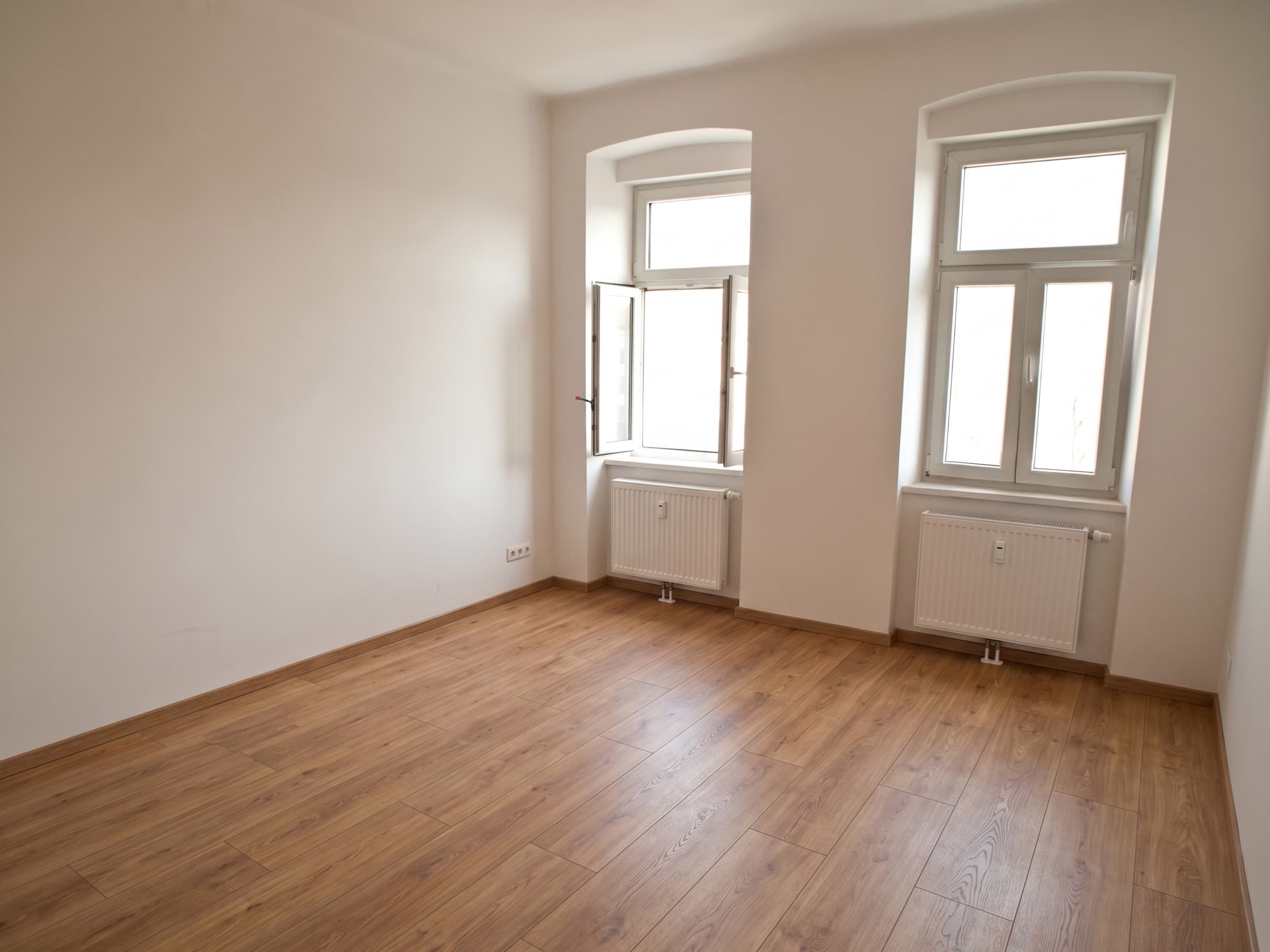Renoviertes Altbauzimmer mit hell gestrichenen Wänden, neuem Laminatboden und zwei Bogenfenstern